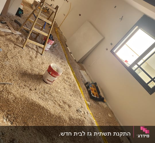 חדר בבנייה עם סולם, דלי וכלי עבודה על הרצפה